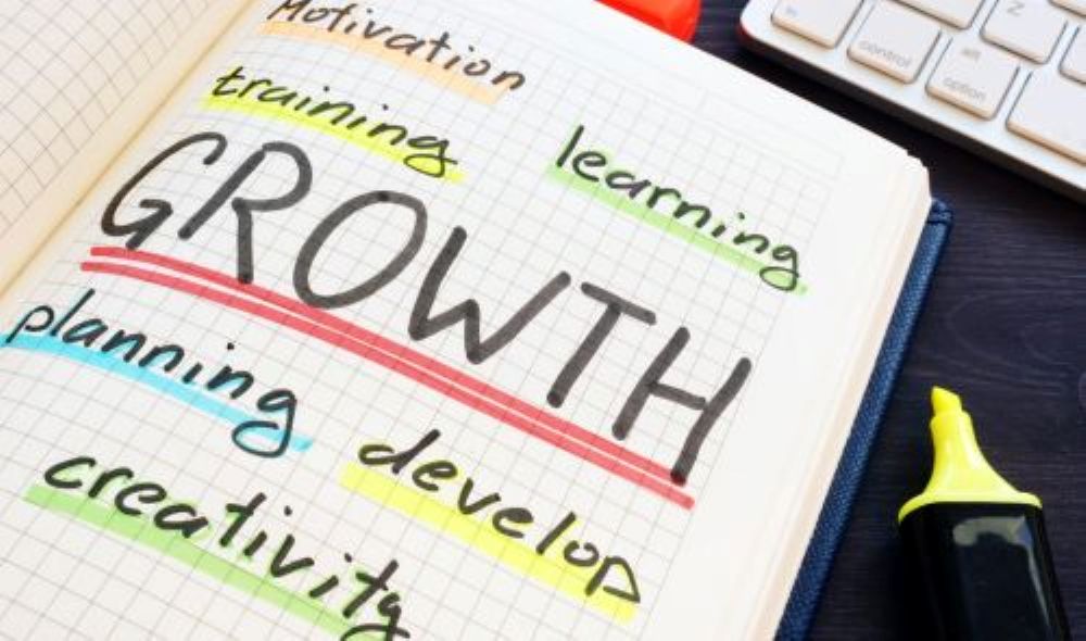 Open notebook showing the word “Growth” in colorful lettering with a development-themed subtitle, with a pencil beside it on a dark desk.